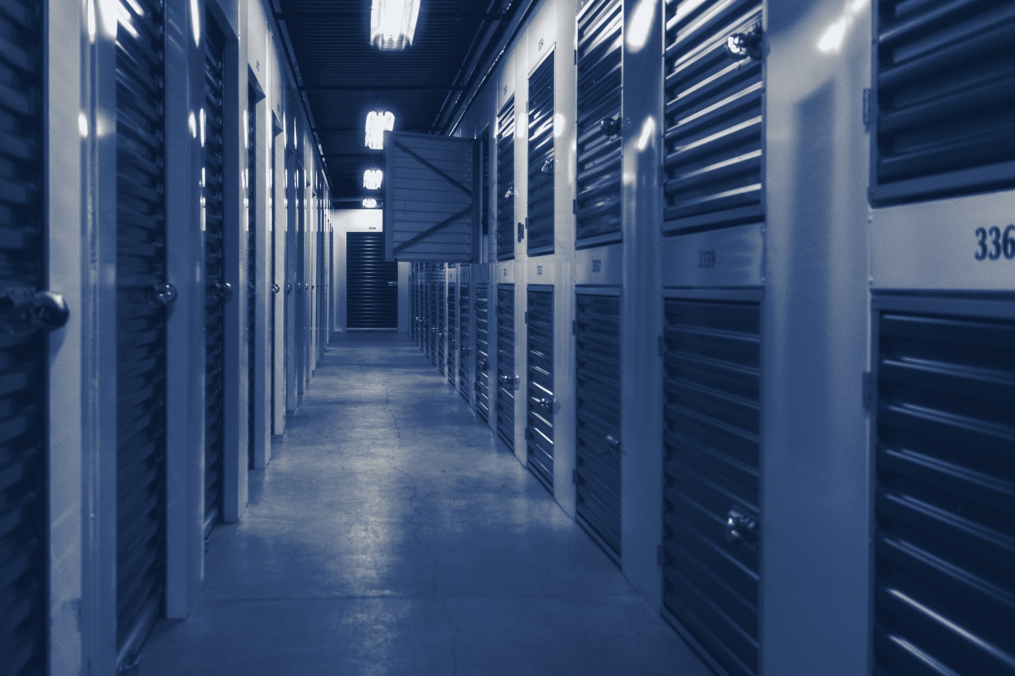 Climate-controlled storage hallway lined with roll-up unit doors and padlocks, tinted navy