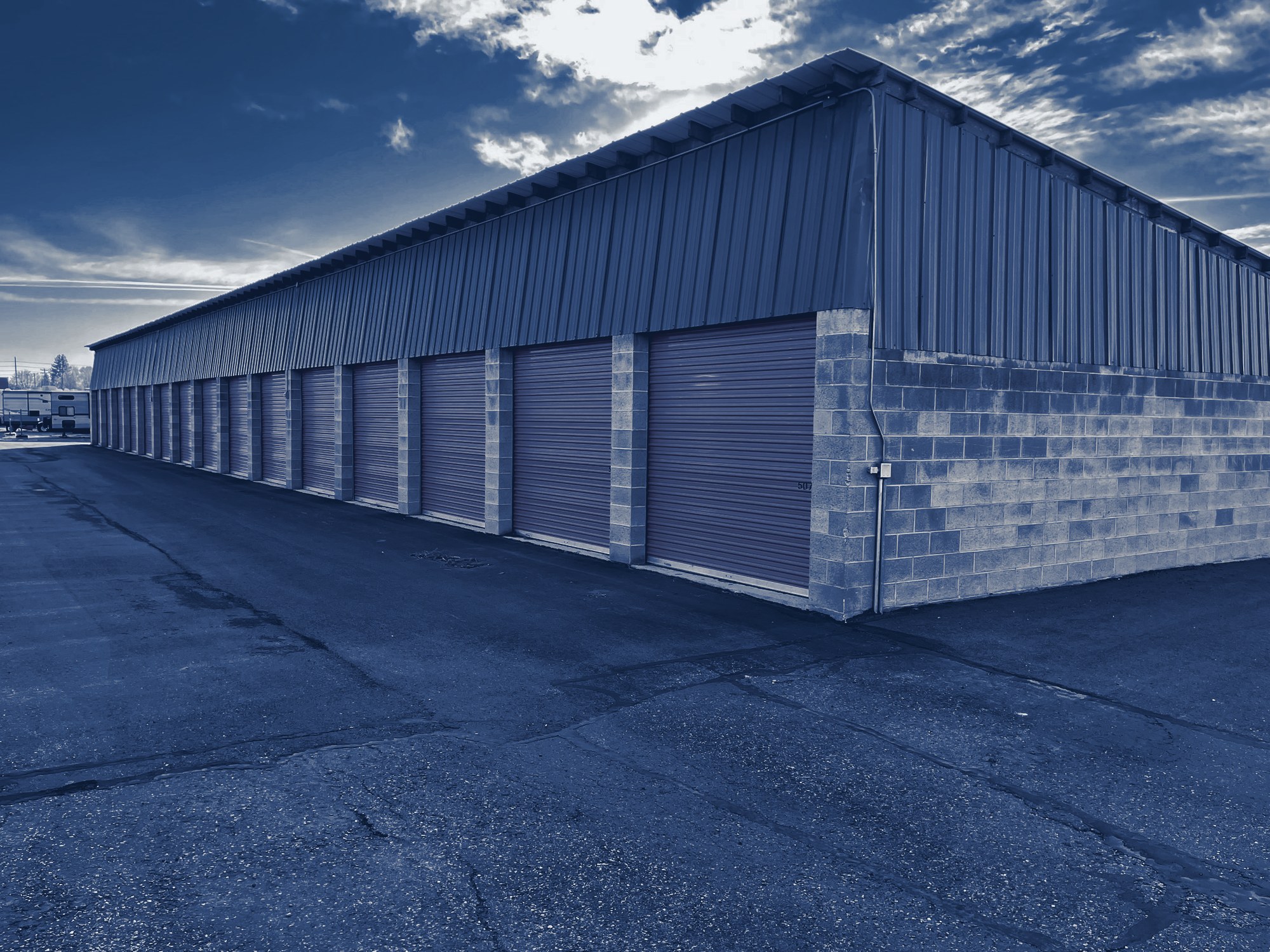 Self-storage building from the drive aisle: long row of roll-up doors and a block end wall, tinted navy