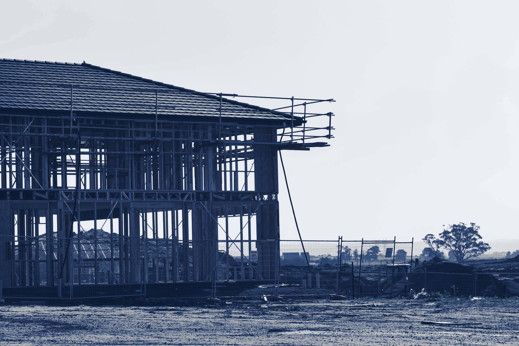New two-story house in timber framing with roof on and scaffolding, on a cleared homebuilding site, tinted navy