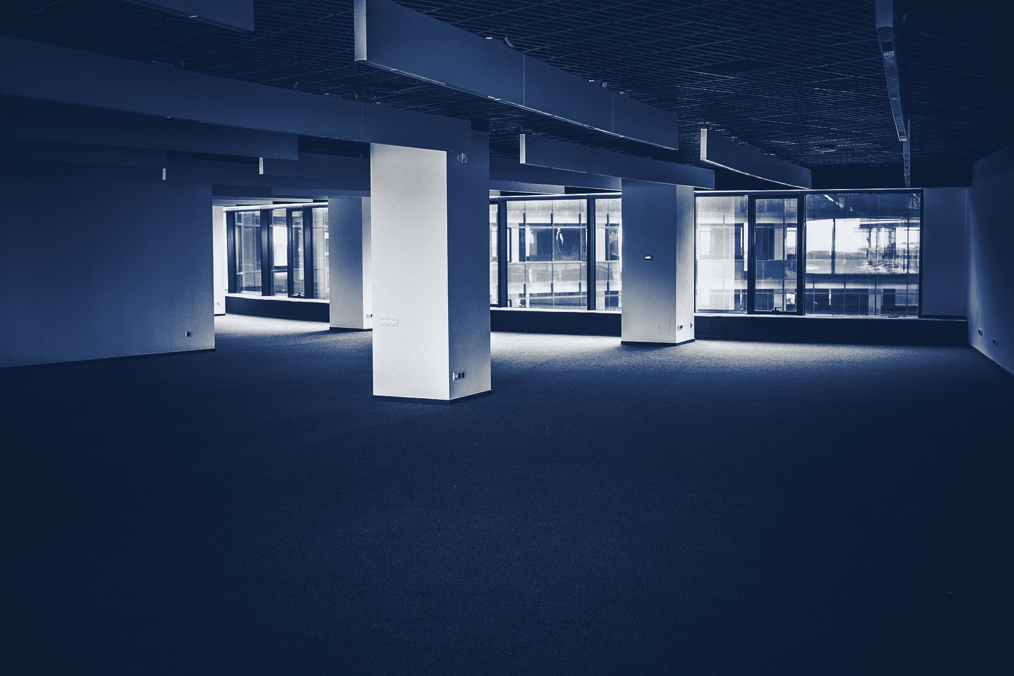 Empty office floor ready for fit-out: open plan, columns, exposed ceiling bulkheads, window wall, tinted navy