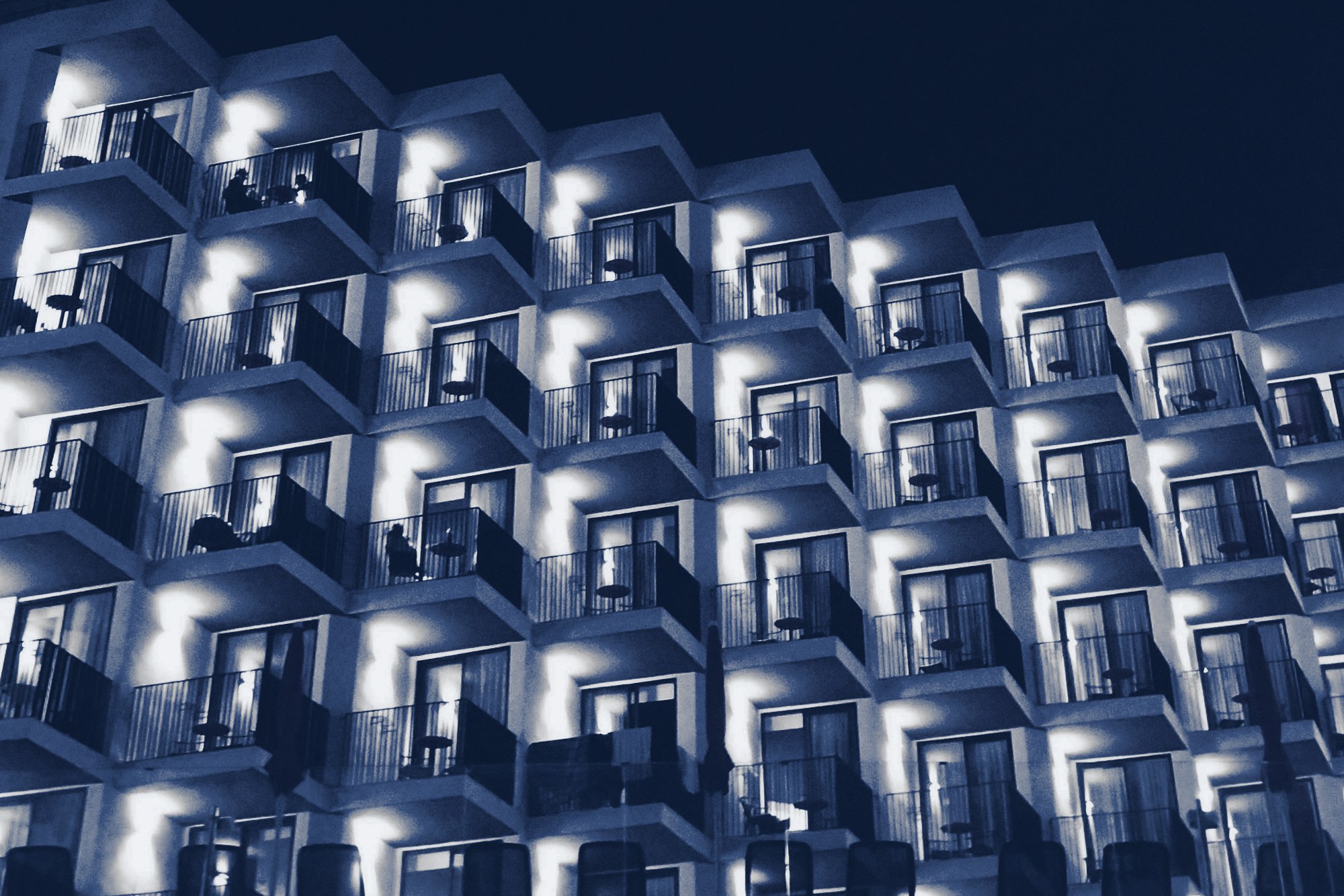Hotel facade at night with rows of lit balconies, tinted navy